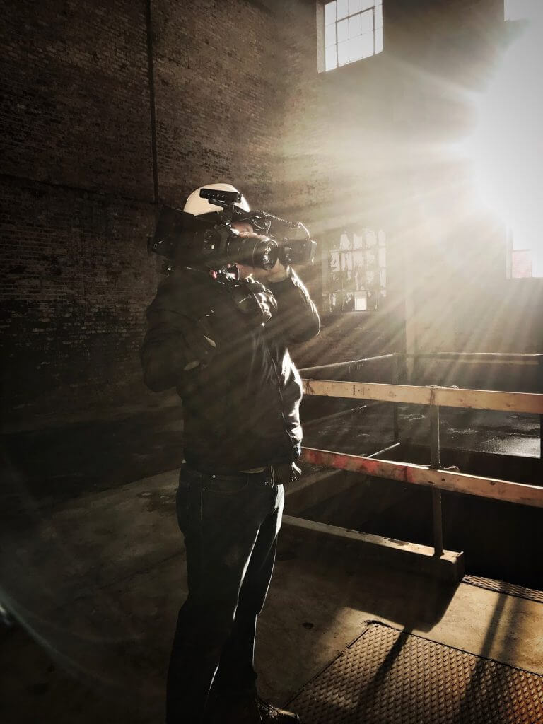 John films in an abandoned warehouse as a light shines into the camera